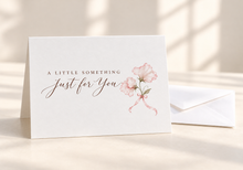 Load image into Gallery viewer, A Little Something Just for You greeting card with two delicate light pink flowers on slender stems tied with a pink bow, beside a white envelope.